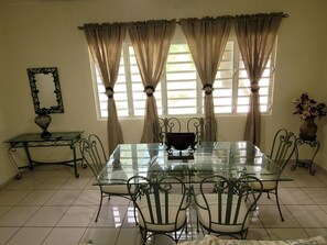 A dining room with a glass table, metal chairs, a vase with flowers, and curtains on the windows.