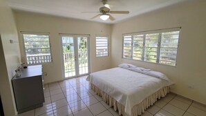 Ein Schlafzimmer mit einem Bett, einem Deckenventilator, einem Schminktisch und großen Fenstern.