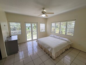 Ein Schlafzimmer mit einem Bett, einem Deckenventilator, einem Schminktisch und großen Fenstern.