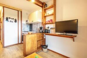 Eine kompakte Küche mit Holzausstattung, einer Mikrowelle, einer Kaffeemaschine und einem an der Wand befestigten Fernseher.