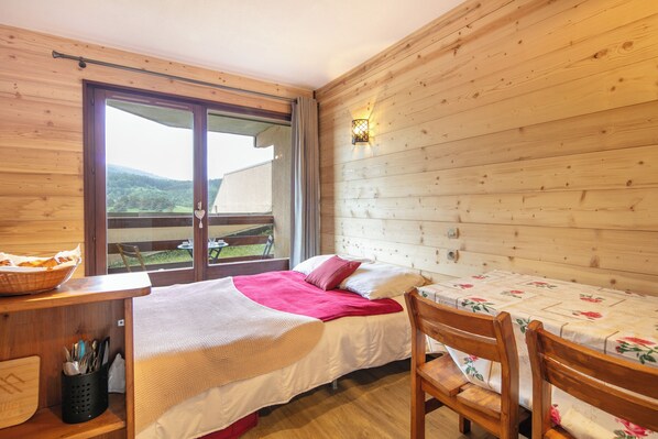 Een kamer met houten vloer, een bed, een tafel en een raam.