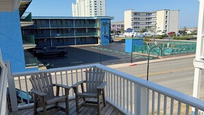 A wooden deck with Adirondack chairs, a view of a hotel with a blue facade, and a parking lot with vehicles.