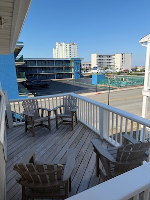 A wooden deck with Adirondack chairs, a view of a hotel with a blue facade, and a parking lot with vehicles.