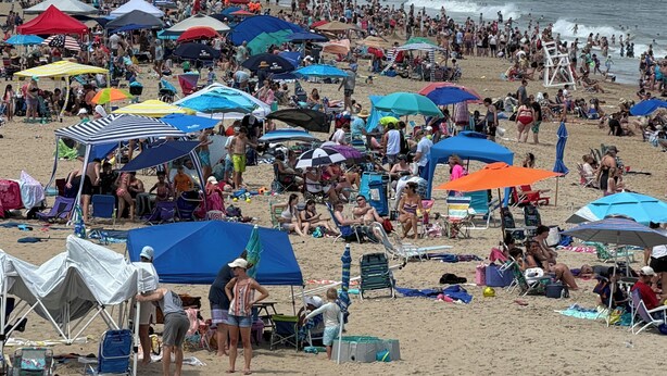 A crowded beach with numerous umbrellas and beachgoers.