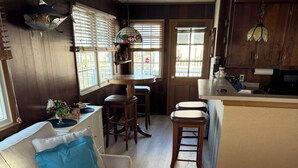 A cozy living room with a sofa, a dining area with a table and chairs, and a kitchen area with wooden cabinets and a hanging light fixture.