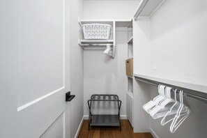 Un couloir étroit avec un étagère en métal, un panier à linge blanc et un plancher en bois.