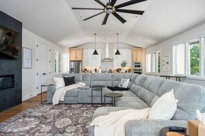 Una sala de estar moderna con un sofá modular, una chimenea y una cocina al fondo.