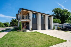 Una casa moderna de dos pisos con balcón, puertas de garaje y un césped bien cuidado.