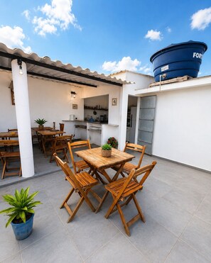 Um pátio externo com mesa e cadeiras de jantar, um reservatório de água azul e uma área de cozinha.