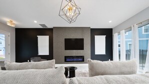 Ein modernes Schlafzimmer mit Kamin, Flachbildfernseher und einer geometrischen Leuchte.