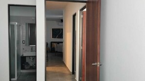 Een hal met een houten deur, een badkamer met een wastafel en een bed op de achtergrond.