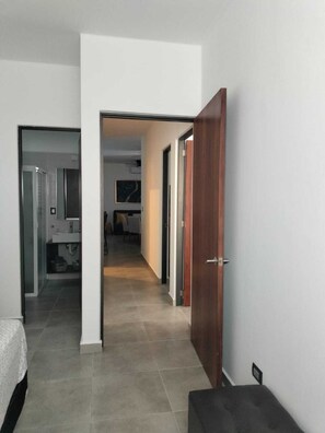 A hallway with a wooden door, a bathroom with a sink, and a bed in the background. - Family Condo with Pool | Near Beach & 5th Ave | Sleeps 6-8 (Playa del Carmen)