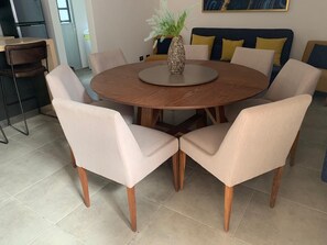 A round dining table with six chairs, a vase with green foliage, and a sofa with yellow cushions in the background. - Family Condo with Pool | Near Beach & 5th Ave | Sleeps 6-8 (Playa del Carmen)