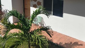 Een gebouw met twee verdiepingen, een balkon, een raam met uitzicht en een kleine tuin met een palmboom.