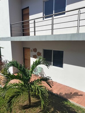 A two-story building with a balcony, a window with a view, and a small garden area with a palm tree. - Family Condo with Pool | Near Beach & 5th Ave | Sleeps 6-8 (Playa del Carmen)