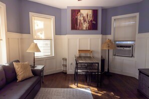 A living room with a sofa, a table, a lamp, and a painting on the wall. - Cozy 1 Bedroom Apartment Near Manhattan & Newark Airport (Jersey City)