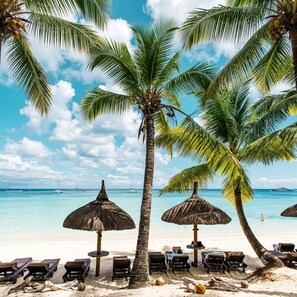 A beach with palm trees, lounge chairs, and thatched umbrellas. - Villa Moony | Private Pool, Rooftop, and Wellness Villa in Mauritius (Trou aux Biches)