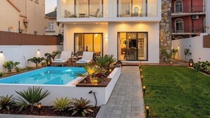 Een modern huis met twee verdiepingen, een zwembad, terras en een verzorgde tuin.