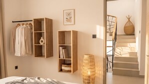 Een slaapkamer met een bed, een kledingkast, een plank met boeken, een vaas en een trap naar een andere kamer.