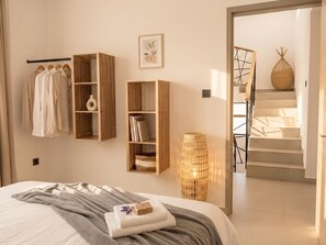 A bedroom with a bed, a wardrobe, a shelf with books, a vase, and a staircase leading to another room. - Villa Moony | Private Pool, Rooftop, and Wellness Villa in Mauritius (Trou aux Biches)