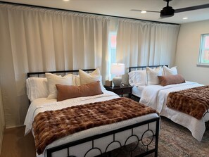 Ein Hotelzimmer mit zwei Betten, einem Deckenventilator und einem fensterbepflanzten Fenster.