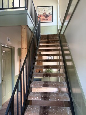 Eine Treppe mit hölzernem Geländer und Metallstreben, die zu einem Raum mit einer Tür und einem gerahmten Bild an der Wand führt.