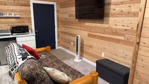 A cozy room with a bed, a TV mounted on the wall, a microwave, and a small kitchenette.