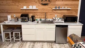 A compact kitchen with a wooden wall, a globe decoration, a microwave, a toaster, a sink, and a dishwasher.