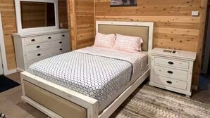 A bedroom with a bed, a dresser, a nightstand, and a wall-mounted TV.