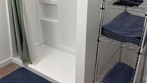 A bathroom with a shower, a towel rack, and a blue rug.