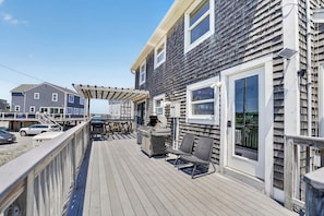 Une terrasse en bois avec des sièges d’extérieur, une pergola et une grande fenêtre.