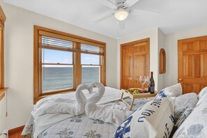 Ein Schlafzimmer mit einem Bett, einem Deckenventilator, Holztüren und Blick auf das Meer.