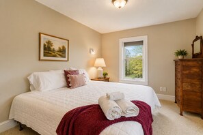 Een slaapkamer met een bed, kussens, een nachtkastje, een lamp, een raam met uitzicht en een kledingkast.