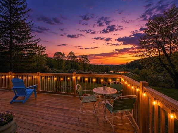 A wooden deck with outdoor furniture and string lights, overlooking a natural landscape.