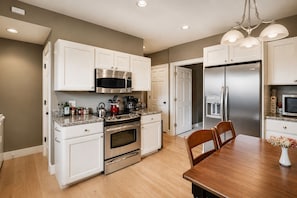 A modern kitchen with white cabinetry, stainless steel appliances, and a wooden dining table.