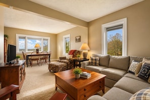 A living room with a sofa, a coffee table, a TV, a dining area with chairs, and a lamp.