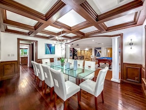 A spacious dining area with a glass table and white chairs, wooden ceiling beams, and a pool table in the background. - Heated Pool & Hot Tub! Pool Table+Close To Beach! (Fort Lauderdale)