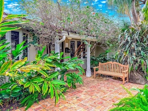 A garden with a wooden bench, a brick pathway, and various plants. - Heated Pool & Hot Tub! Pool Table+Close To Beach! (Fort Lauderdale)