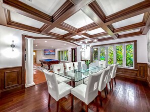 A spacious room with a glass-top dining table surrounded by white chairs, a pool table, and large windows with a view of greenery. - Heated Pool & Hot Tub! Pool Table+Close To Beach! (Fort Lauderdale)