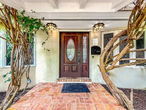 A front entrance with a wooden door, a welcome mat, and two light fixtures. - Heated Pool & Hot Tub! Pool Table+Close To Beach! (Fort Lauderdale)