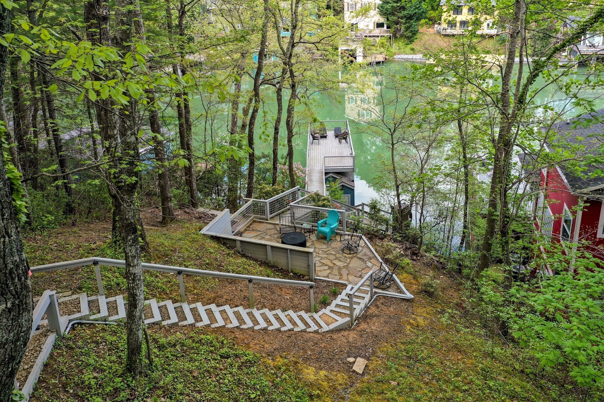A wooden deck with a staircase leading to a viewing platform, surrounded by trees and overlooking a body of water.