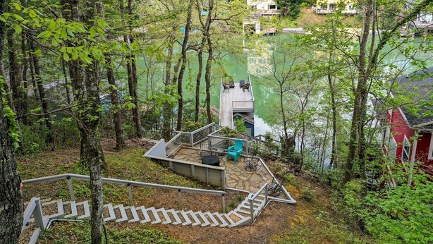 Une terrasse en bois avec un escalier menant à une plateforme d’observation, entourée d’arbres et donnant sur une étendue d’eau.