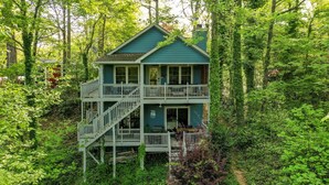 Une maison à deux étages dotée d’un balcon, entourée d’une forêt dense.