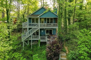 A two-story house with a balcony, surrounded by dense forest.