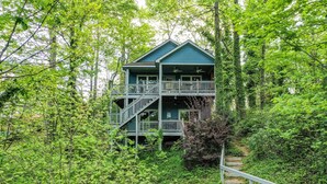 Un chalet à deux étages doté d’un balcon, entouré d’une forêt dense.