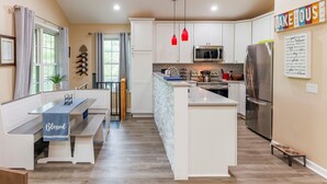 Une cuisine moderne avec des meubles blancs, un îlot central, un coin repas avec un banc et une enseigne indiquant « Lake House ».
