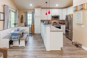 A modern kitchen with white cabinets, a central island, a dining area with a bench, and a 'Lake House' sign.