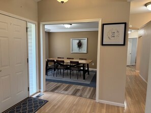 Un pasillo que conduce a un comedor con una mesa y sillas, un cuadro en la pared y una puerta a la izquierda.