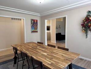 A dining area with a long wooden table, chairs, and a painting on the wall.