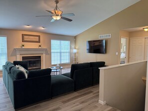 Una sala de estar con chimenea, ventilador de techo, televisor de pantalla plana y una escalera que sube a otro nivel.